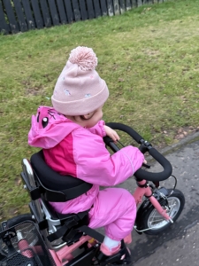Flickan Caledonia cyklar på sin momo trehjuling.