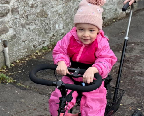 Flickan Caledonia cyklar på sin momo trehjuling.