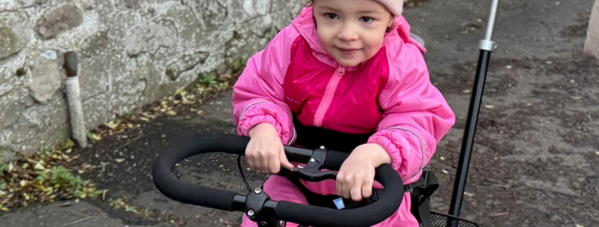 Flickan Caledonia cyklar på sin momo trehjuling.